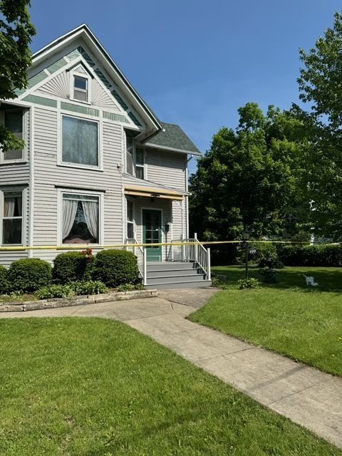 Two-story house with gray siding, a front porch, and yellow police tape in front of it.