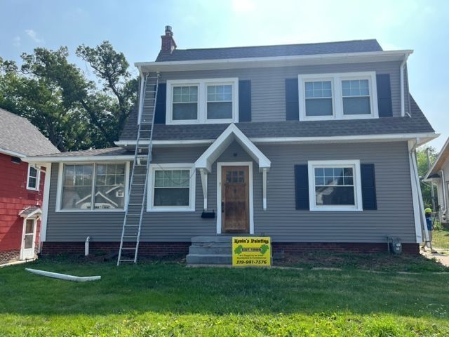 Gray two-story house with white trim, blue shutters, and a ladder. A sign is in the front yard.