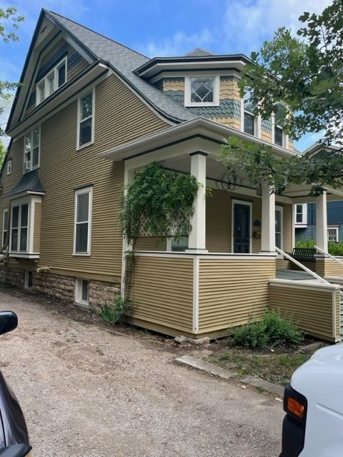 Two-story house with yellow siding, porch, and green trim; stone foundation and a light-colored driveway.