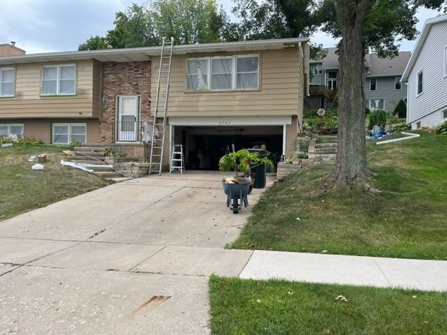 Two-story house with tan siding, open garage, ladder, and a dog on the driveway.