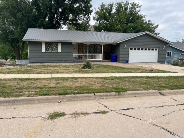 Gray house with white garage door, front porch, and blue trash can.