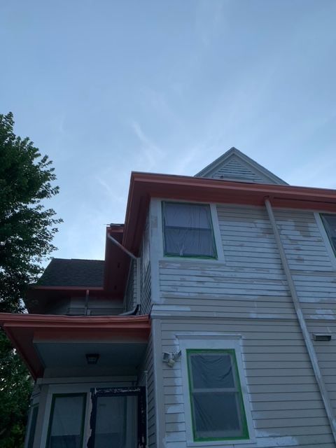 Exterior view of a house with peeling paint and orange trim. Under a blue sky.