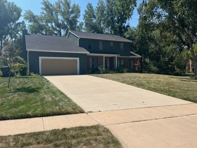 Two-story house with a dark gray exterior, beige garage door, and a long concrete driveway on a sunny day.