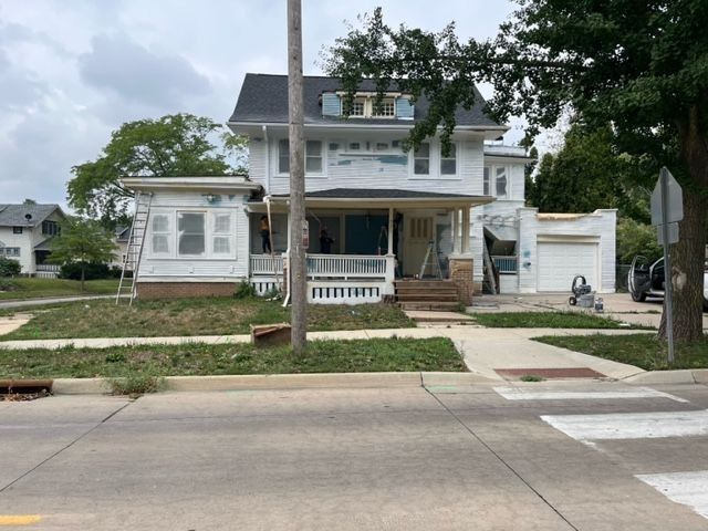 Two-story white house under construction, front porch, garage, on a residential street.