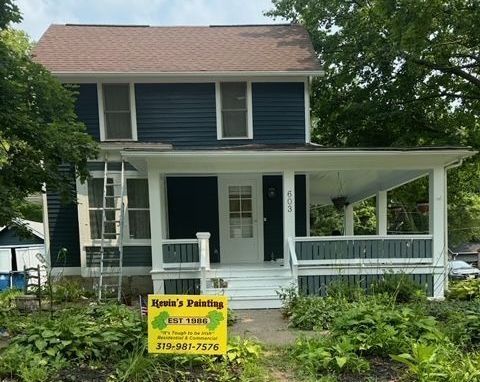 Two-story house with dark blue siding, white trim, and a porch, with a painter's sign in front.