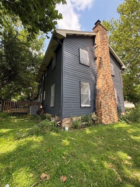 Two-story house with dark blue siding, a brick chimney, and a green yard.