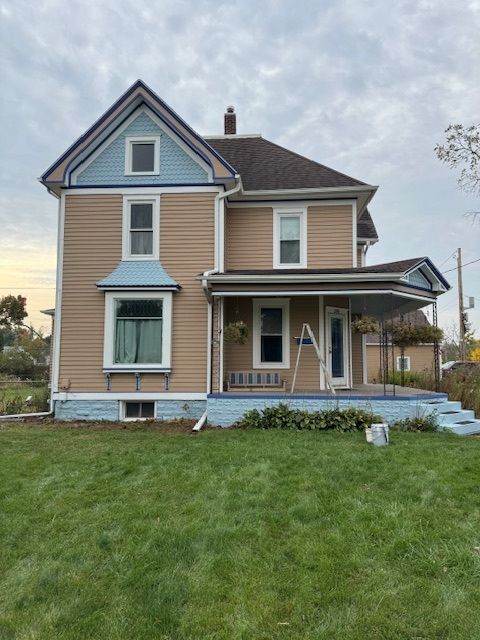 Two-story beige house with blue trim, green lawn, cloudy sky.