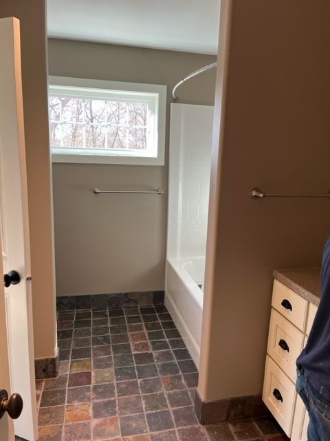 Bathroom with slate floor, white tub, window, and neutral-colored walls.