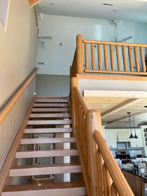 Wooden staircase with log railing leading to a loft, beige walls, kitchen visible below.