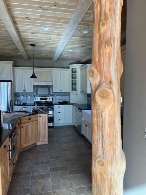 Rustic kitchen with light wood ceiling and a large log column. White cabinets, black countertops.
