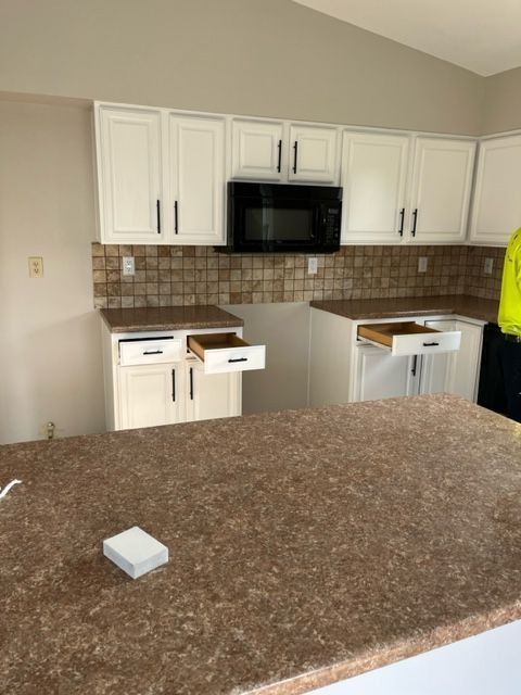 White kitchen cabinets, dark countertop, tile backsplash, and microwave. Drawers open.