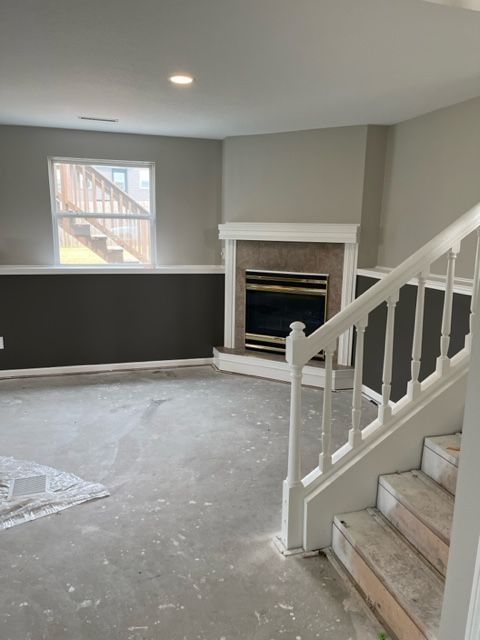 Basement room with dark wainscoting, white staircase, fireplace, and unfinished concrete floor.