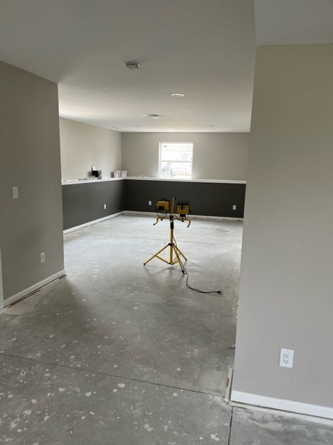 A mostly empty room under construction with dark accent wall, gray floors, and work lights.