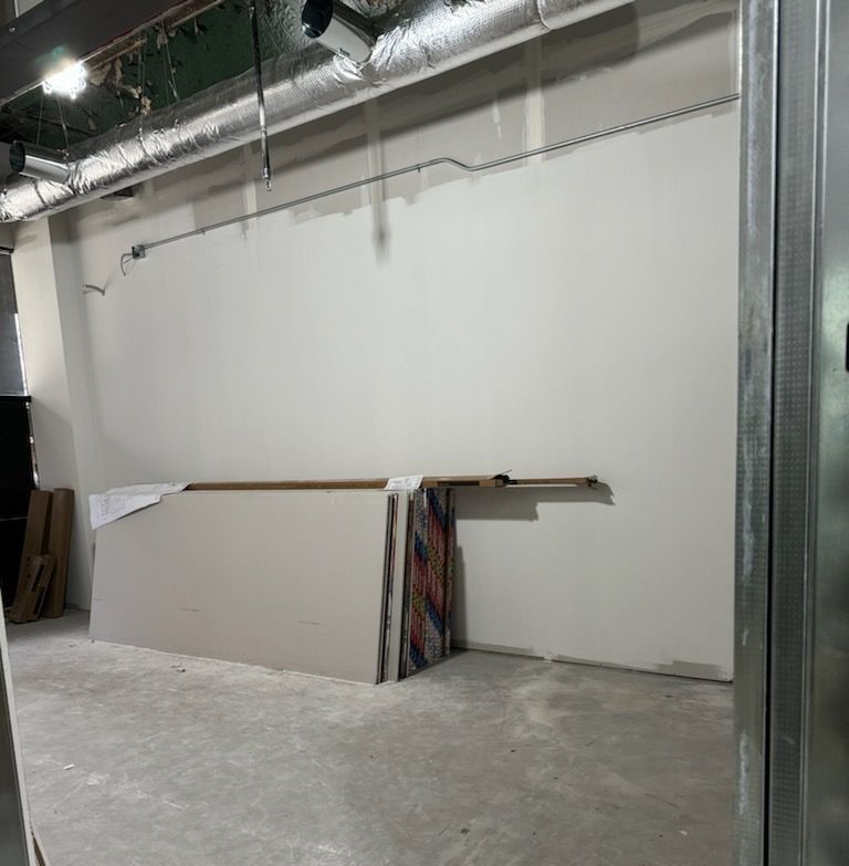 Construction of an interior space with exposed ductwork and a bare wall. Drywall leaning against the wall.
