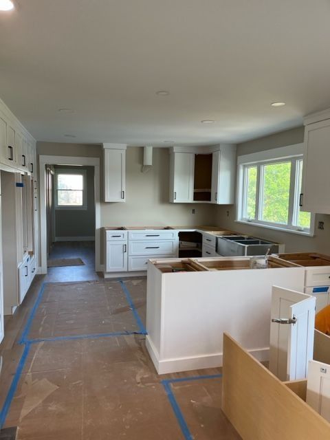 A white kitchen remodel in progress; cabinets installed, island, light walls, and blue tape on the floor.
