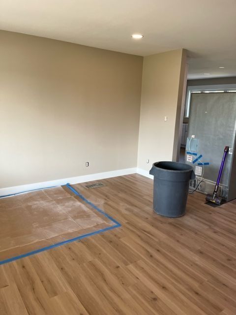 Empty room with tan walls, wood floors, and a gray trash can. Construction debris visible.