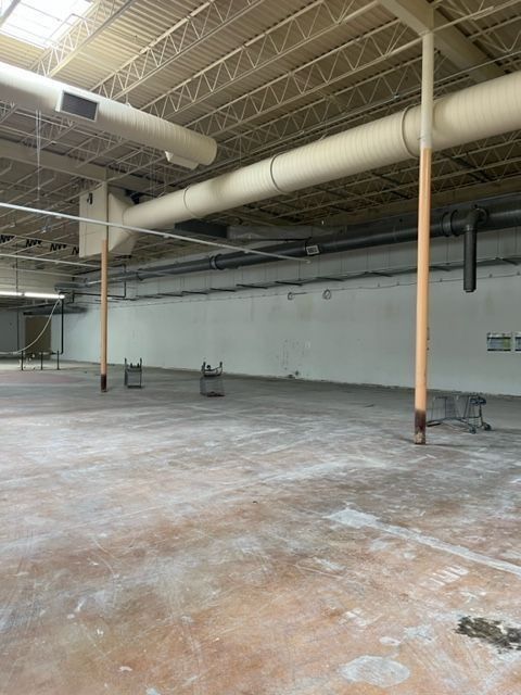 Empty, open-plan commercial space with concrete floor, white walls, and exposed pipes.