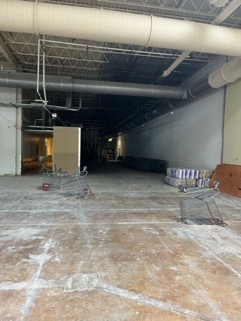 Empty retail space with exposed ceiling, concrete floor, and shopping carts.