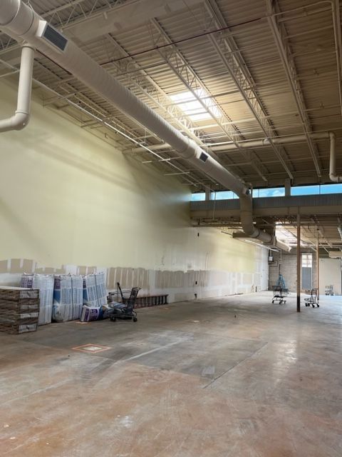 Empty warehouse interior with white walls, exposed ductwork, and construction materials.