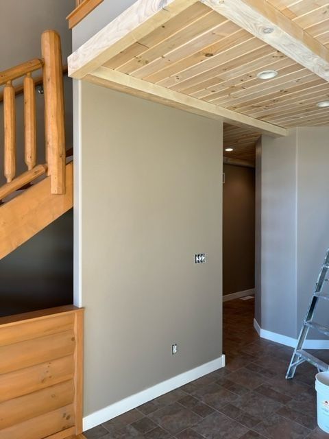 Interior view of a room with a staircase, wooden ceiling, and tan walls. A door leads to another room.
