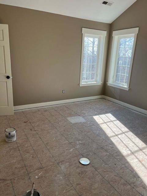 Empty room with beige walls, two windows, and a door. Flooring is unfinished.