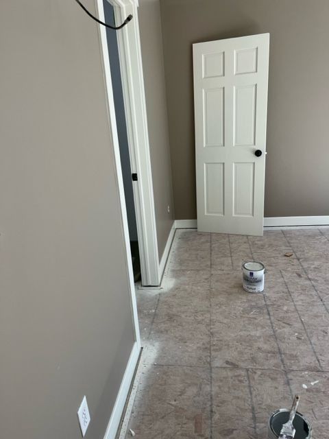 Bedroom with white door, beige walls, and gray floor. Paint can on the floor.