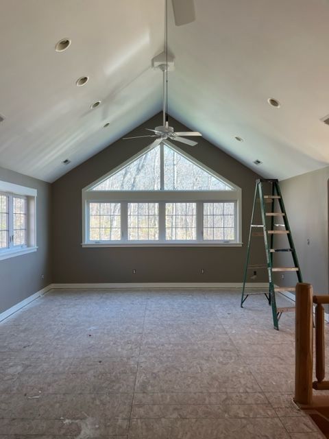 Empty room with high, angled ceiling, large window, and ladder. The walls are gray.