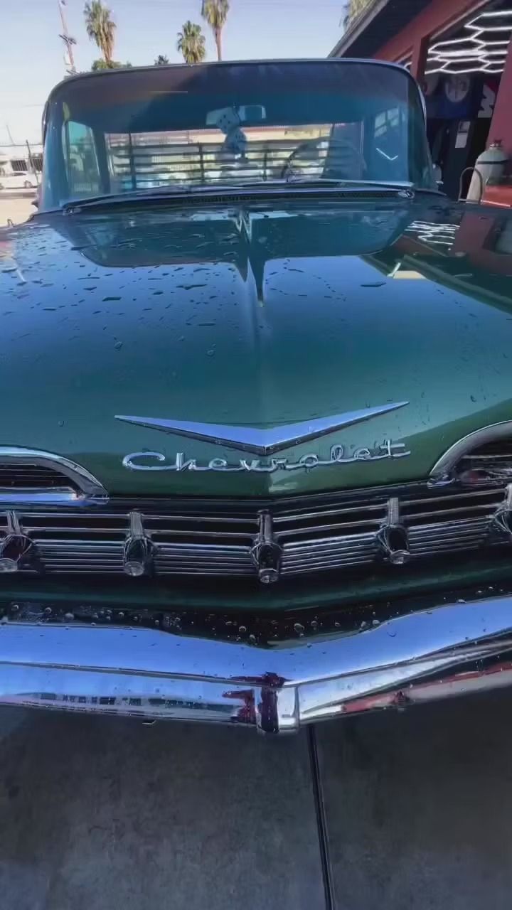 Close-up front view of a shiny green vintage Chevrolet car with chrome trim, parked outdoors on a sunny day.