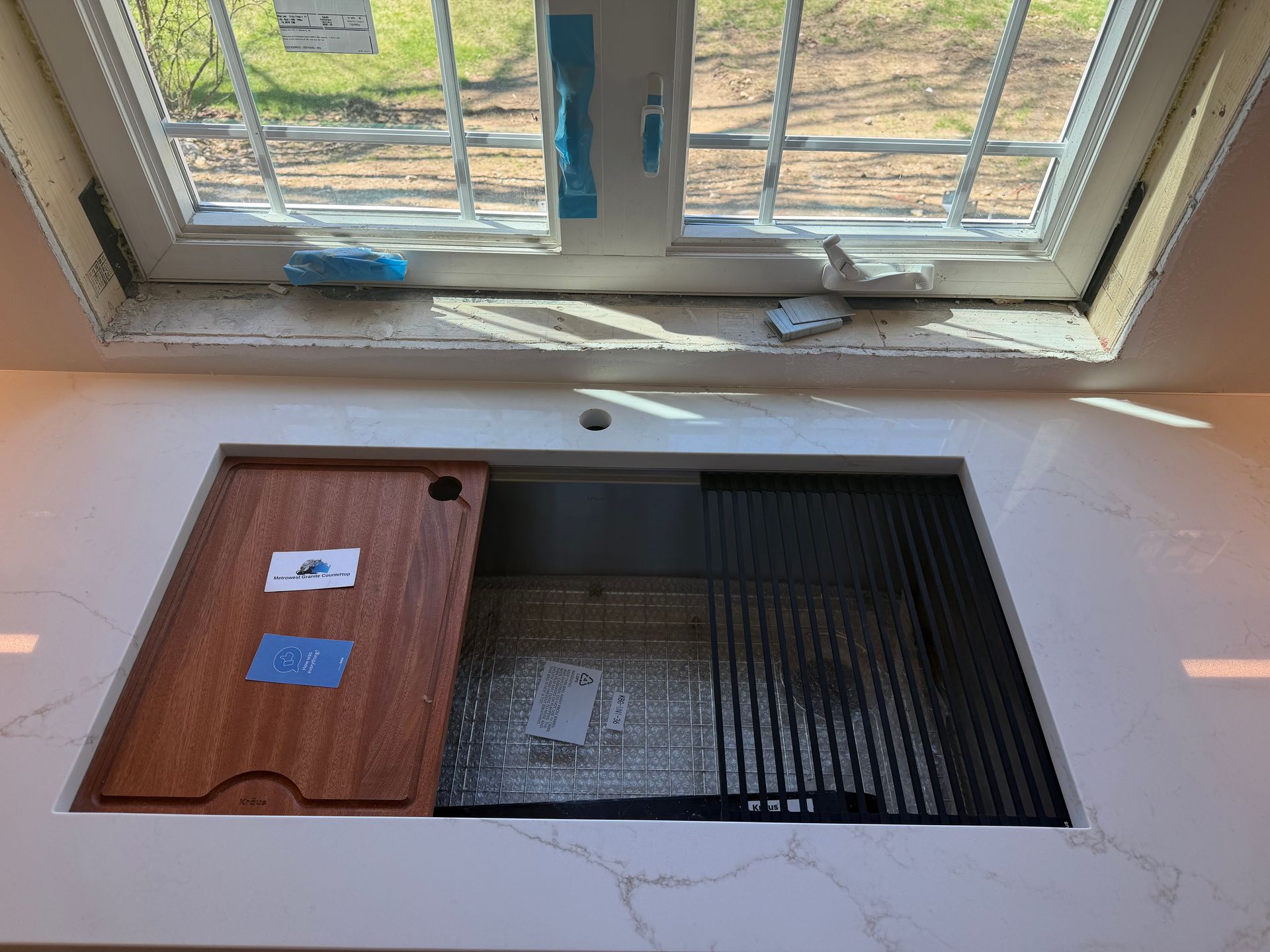 Open floor hatch beside a window, with a wooden cover and dark recessed opening.