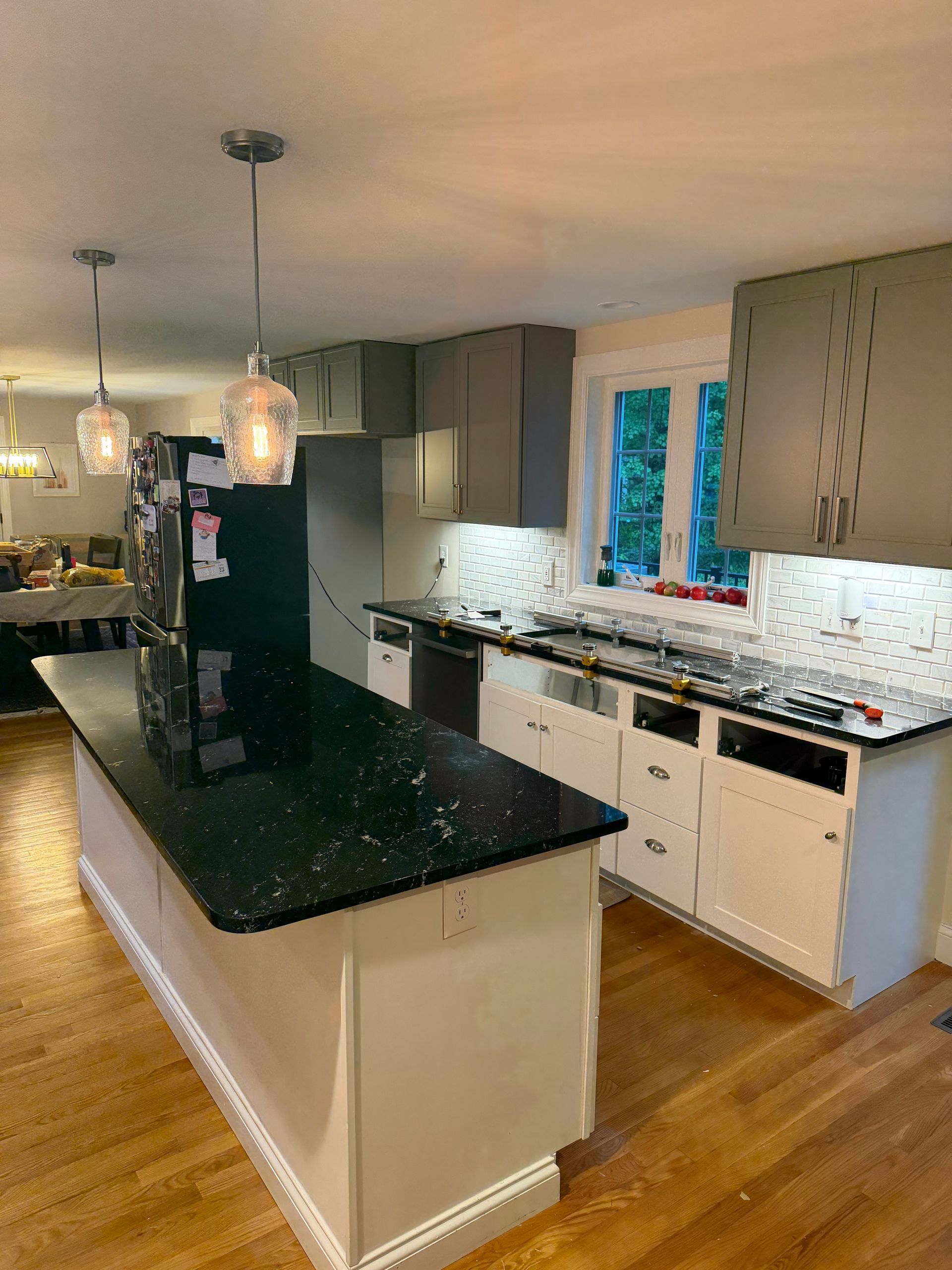 Modern kitchen with black island, white cabinets, pendant lights, and hardwood floors.