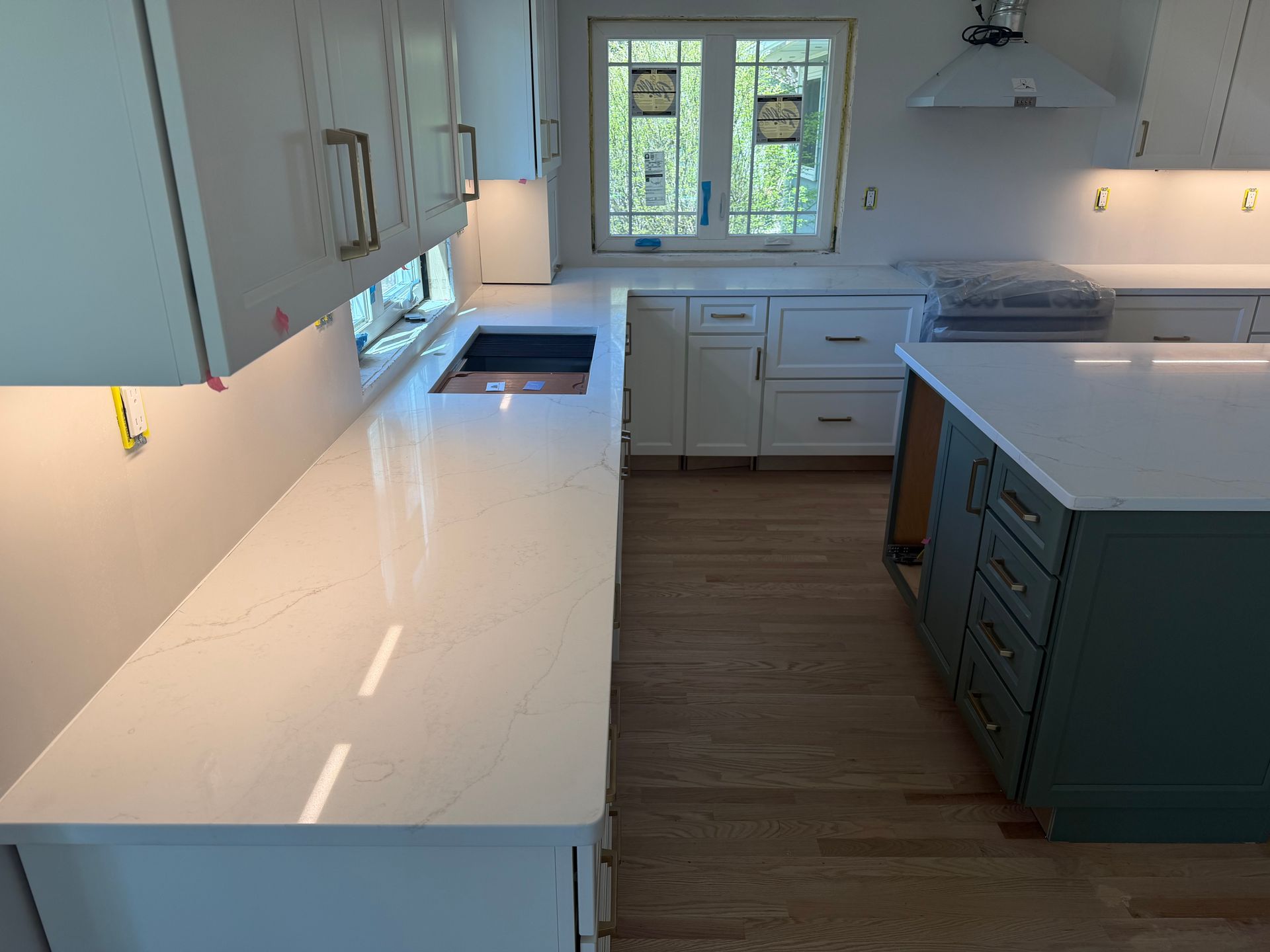 Bright modern kitchen with white countertops, green cabinets, and a window over the sink.