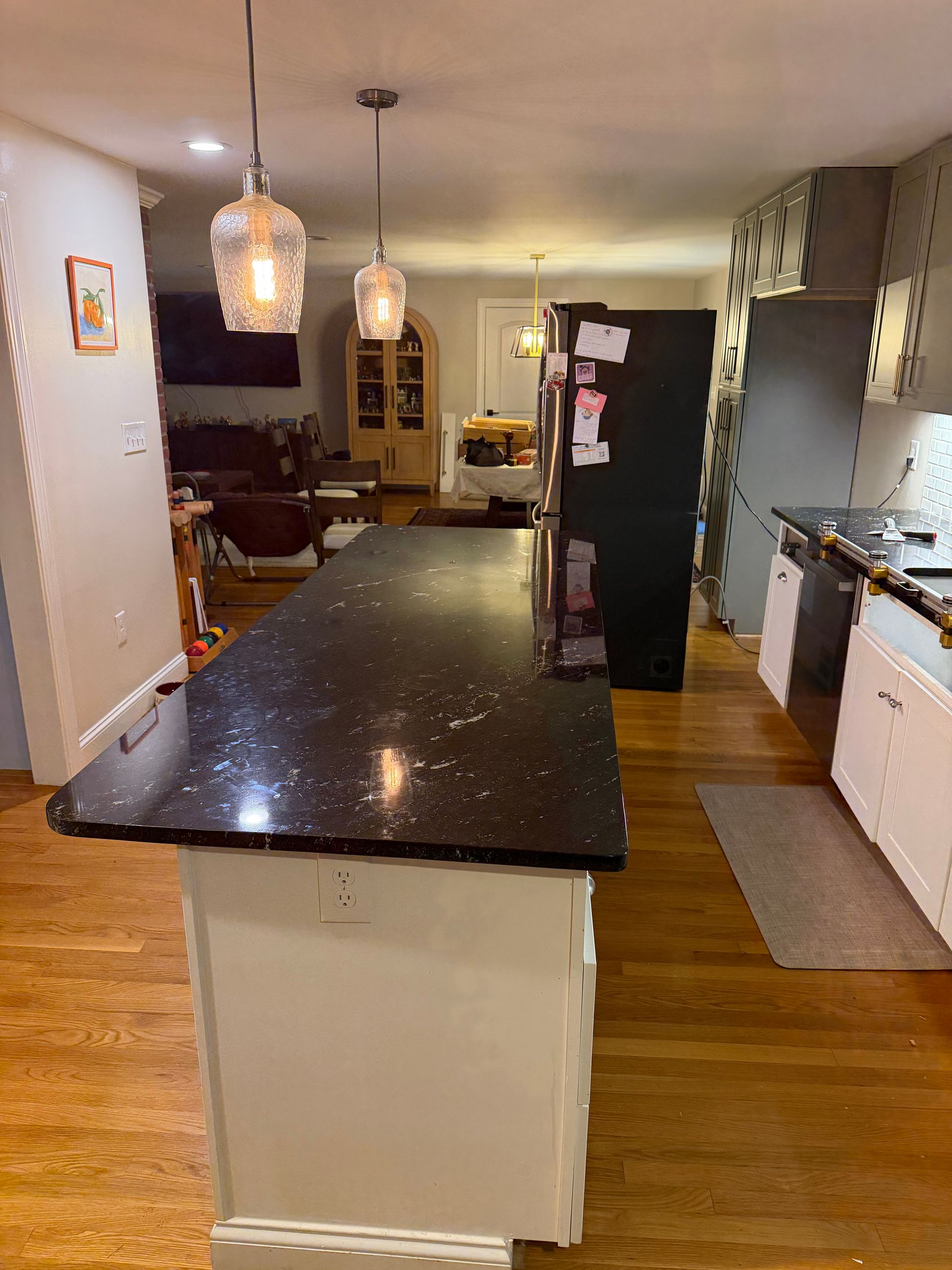 Kitchen with black island countertop, hardwood floors, hanging pendant lights, and cabinets along the right wall.