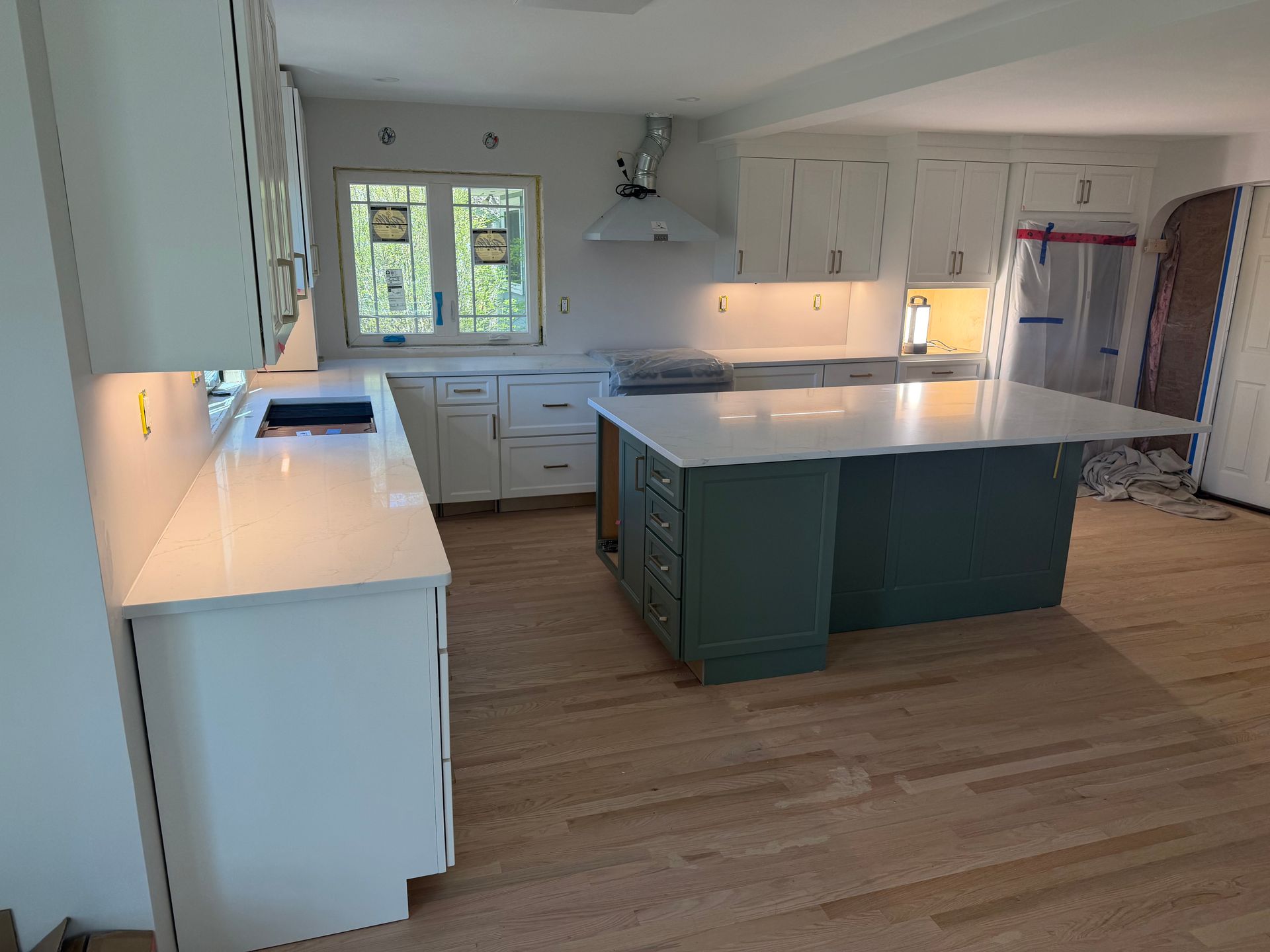 Bright modern kitchen with white cabinets, central island, wood floor, and sunlit window.