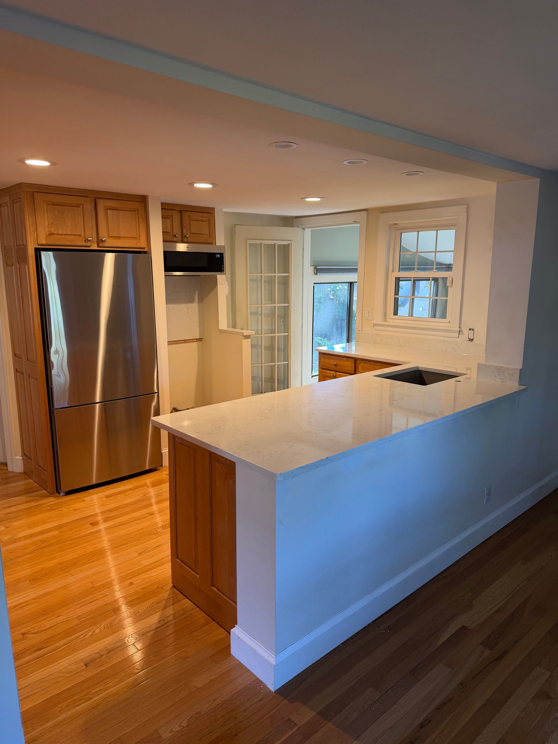Bright kitchen with stainless steel fridge, wood cabinets, white peninsula, and hardwood floors.