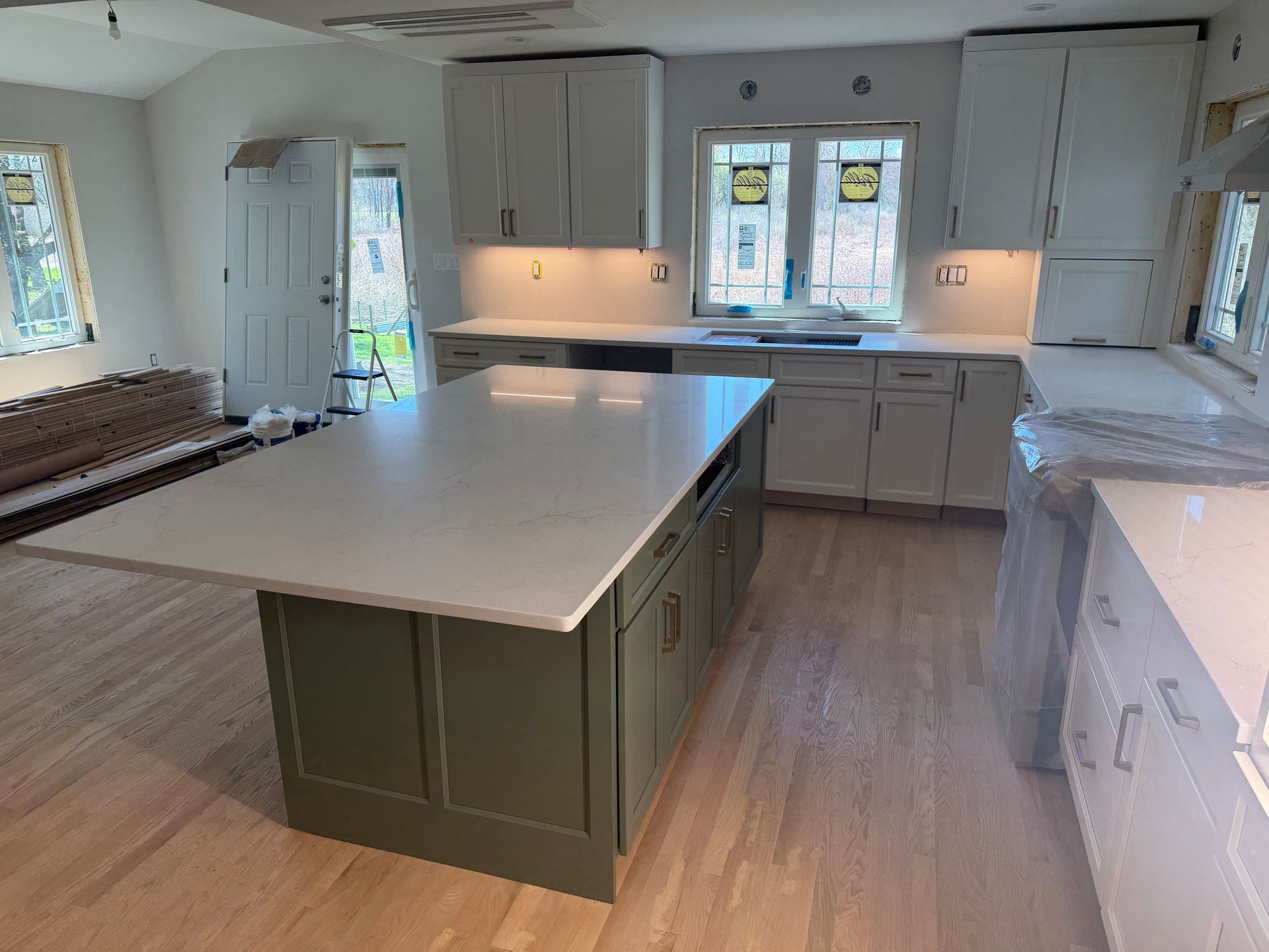 Bright modern kitchen with a large green island, white cabinets, and windows letting in daylight