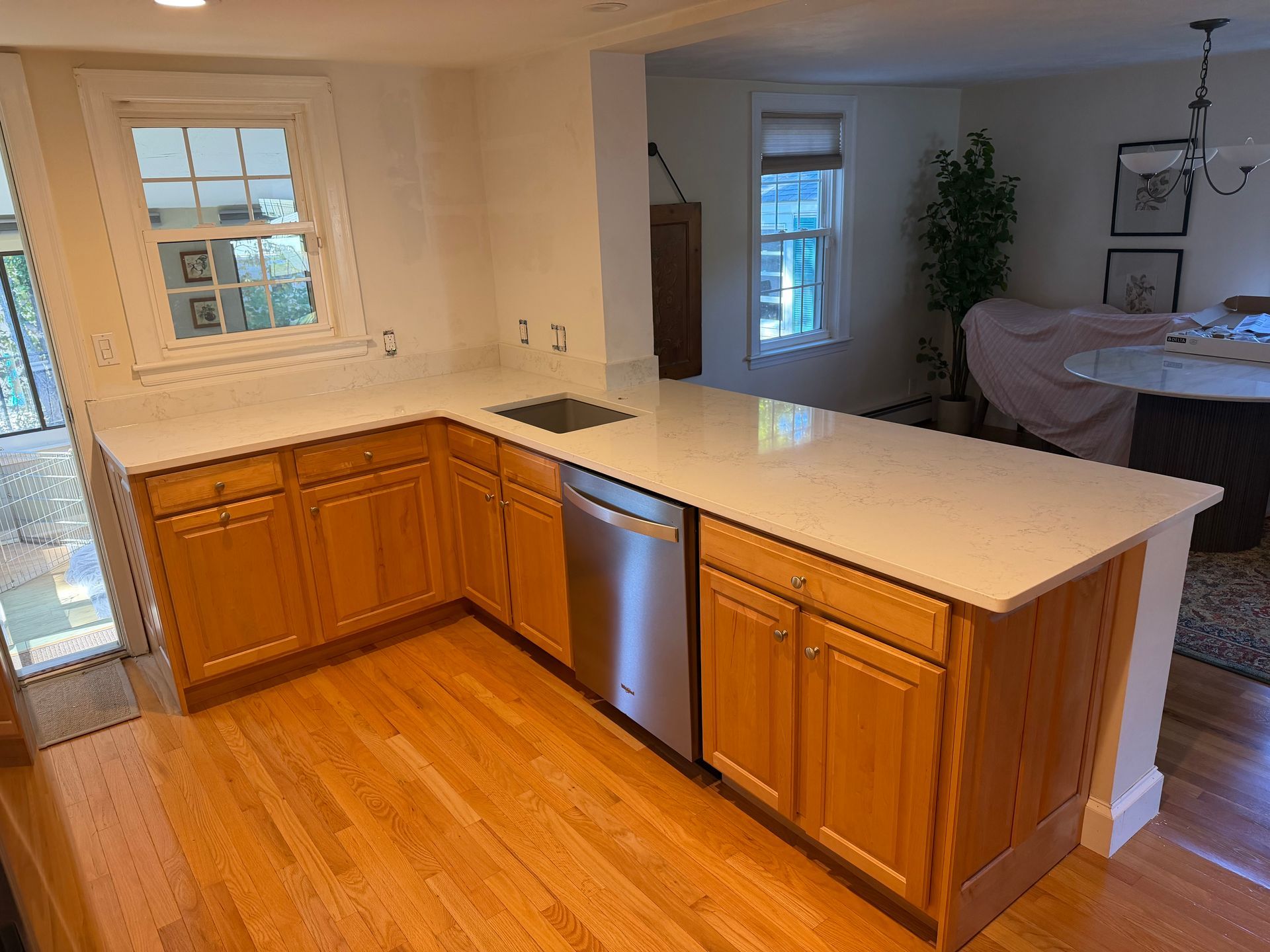 Kitchen with wood cabinets, white countertops, stainless dishwasher, and an open view into a bedroom.
