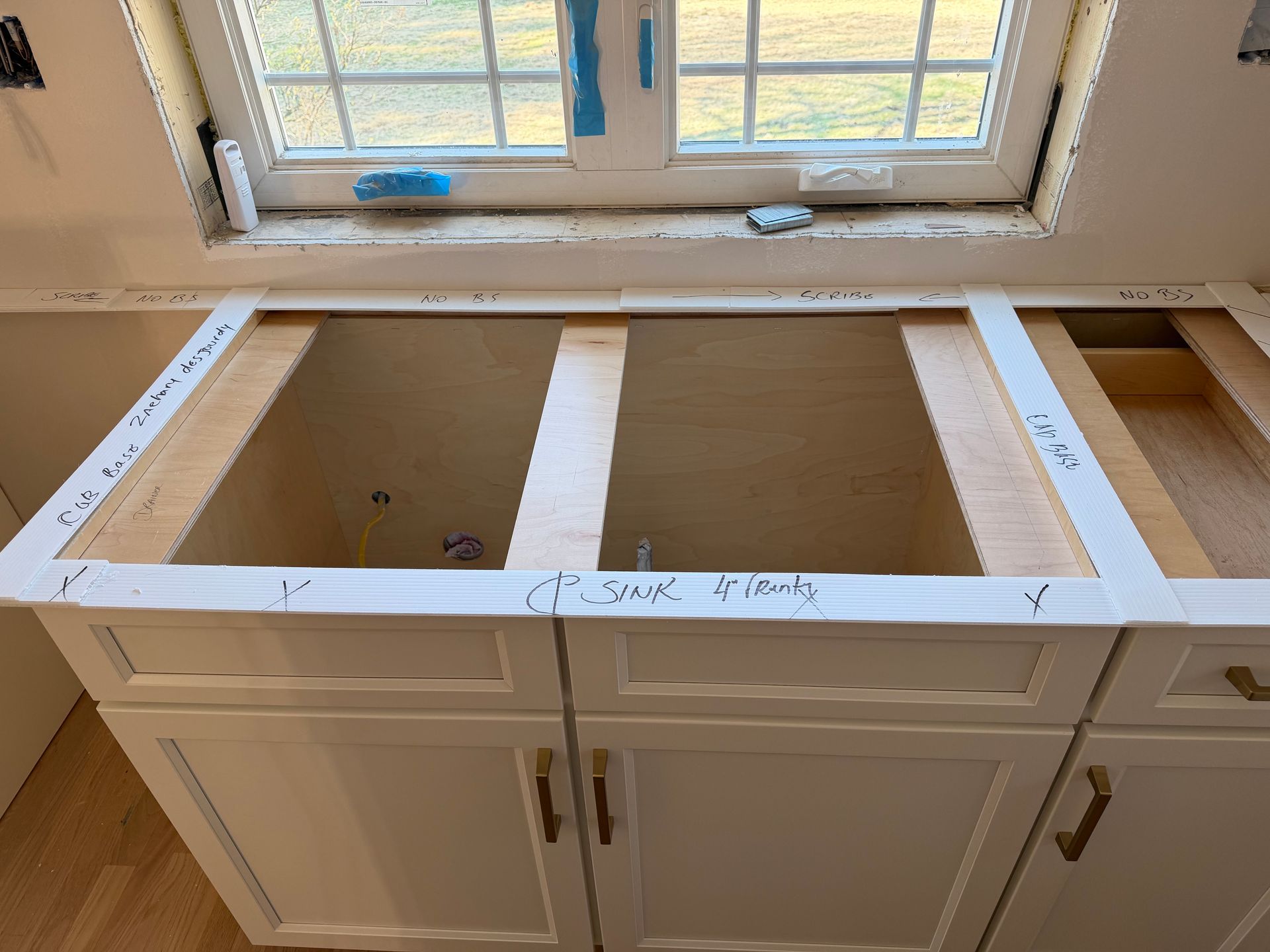 Unfinished kitchen base cabinets with countertop cutout beneath a window, white trim and open center spaces.