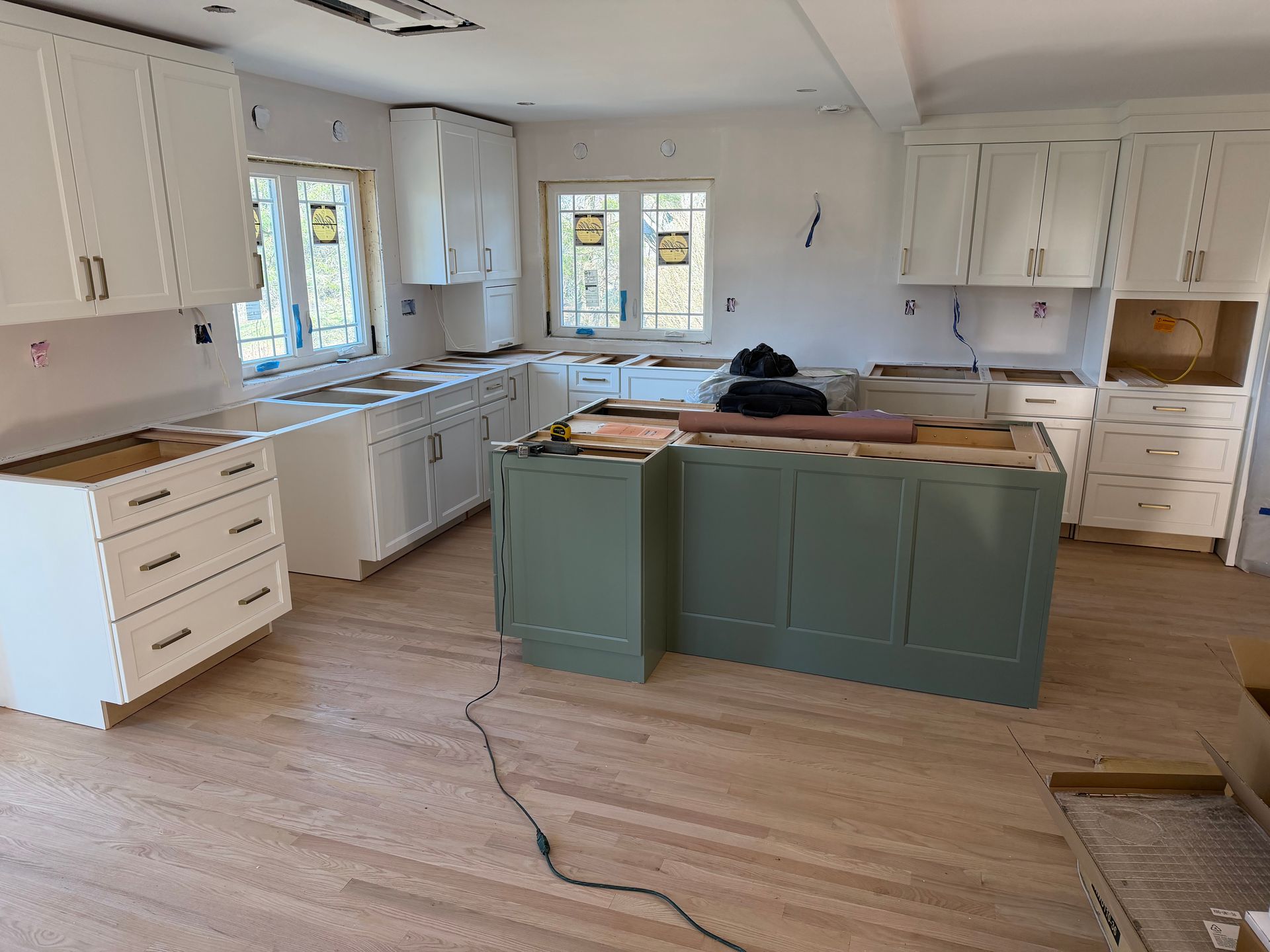 Partially renovated kitchen with white cabinets, teal island, wood floors, and tools on the floor