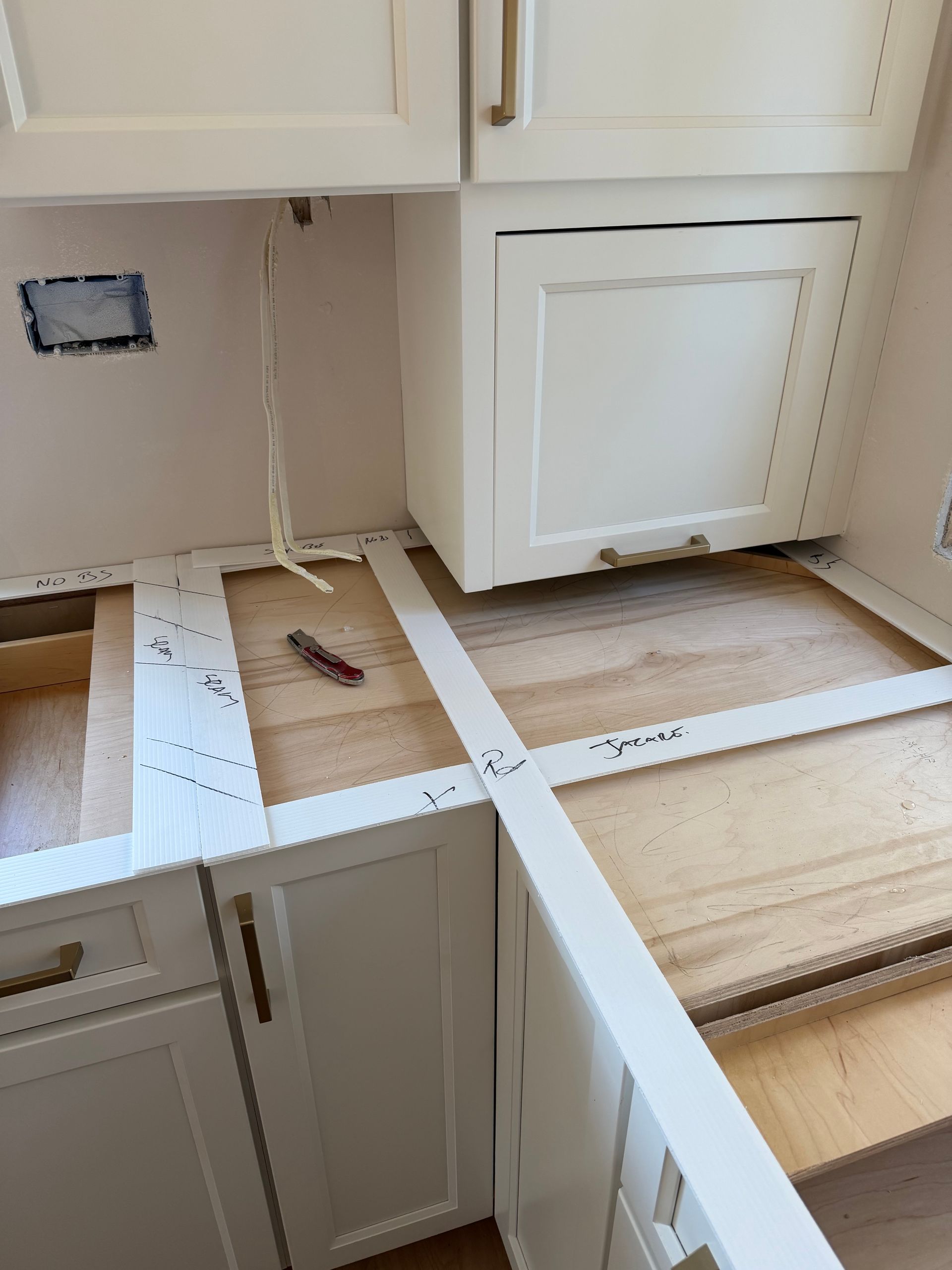 Kitchen under renovation with open floor, exposed subfloor, and white cabinets along the wall