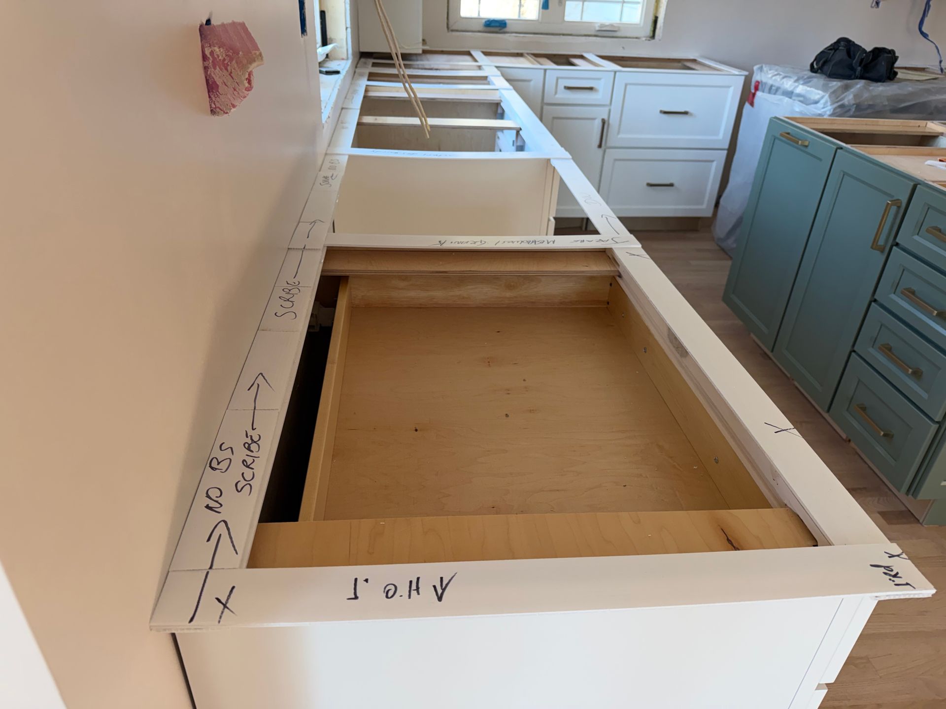 Partially installed white kitchen cabinets with an unfinished wood drawer opening in a bright room