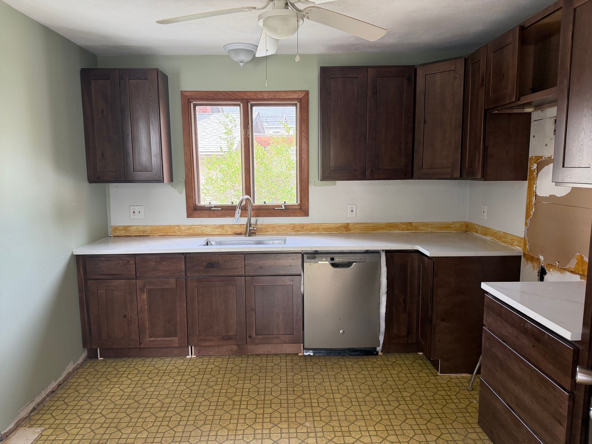 Small kitchen with dark wood cabinets, white walls, window over sink, and unfinished countertop edges.