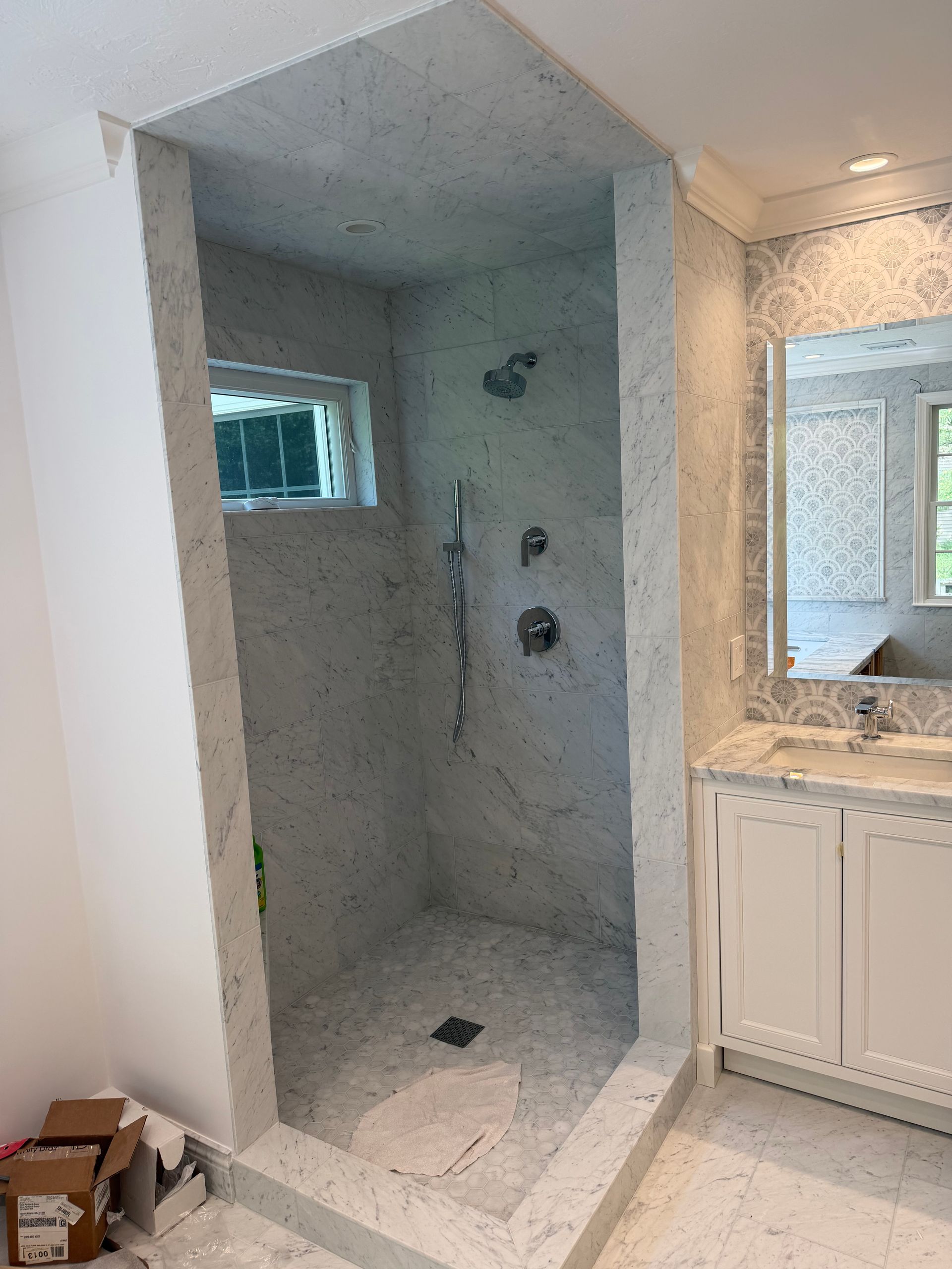 Empty tiled shower stall under construction next to a bathroom vanity and mirror
