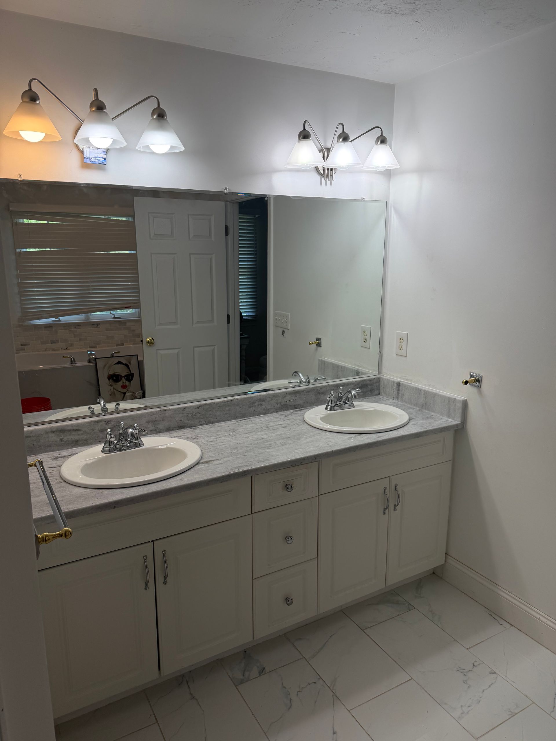 Bright bathroom vanity with double sinks, large mirror, and wall lights above a speckled countertop.