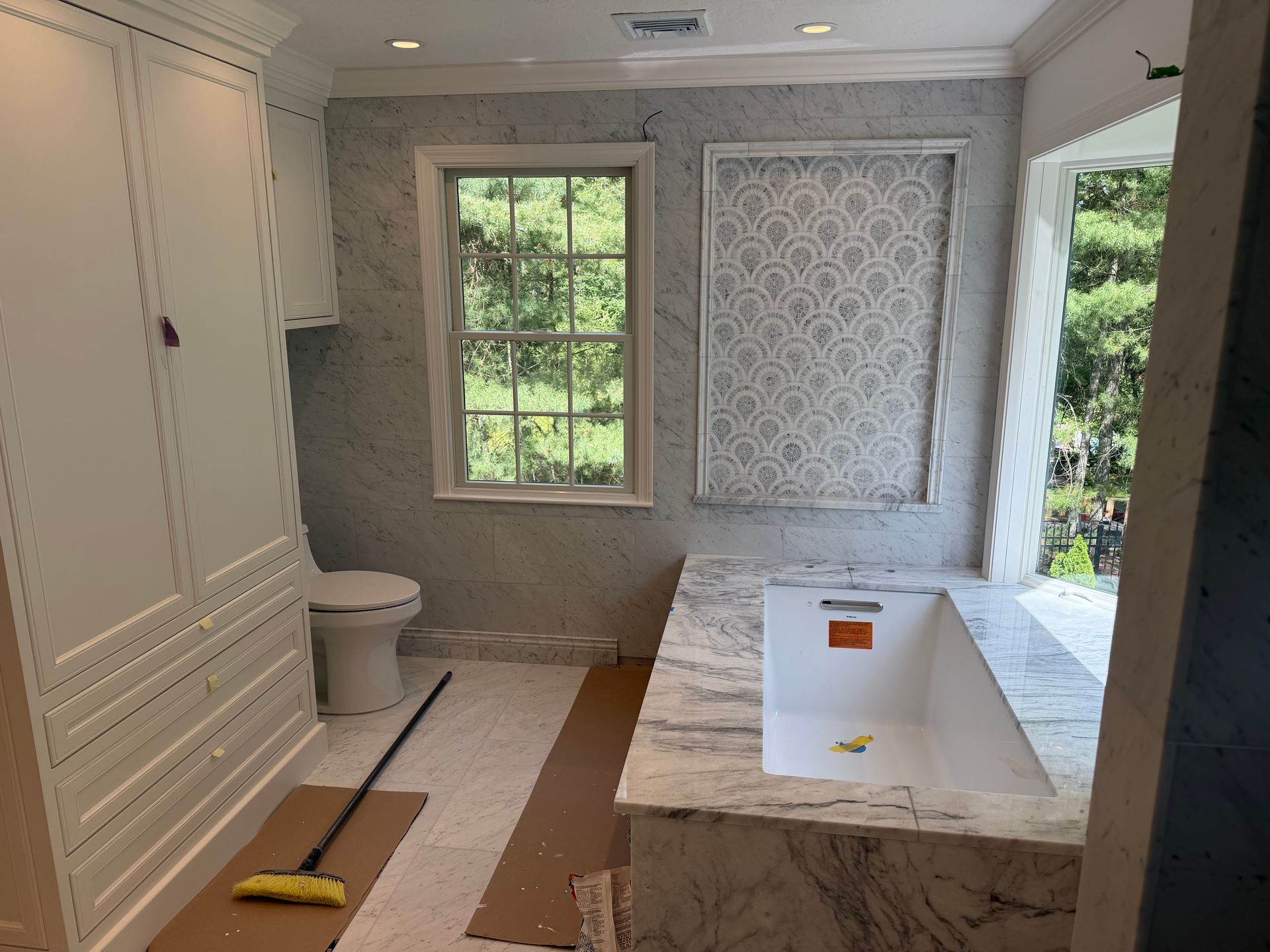 Small bathroom under renovation with gray walls, white tub, vanity, and window with patterned shade.