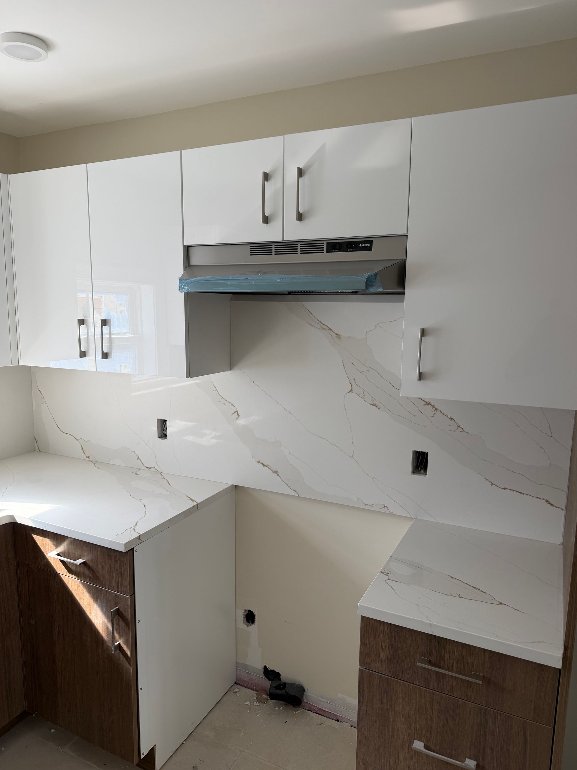 Small white kitchen with upper cabinets, marble-look backsplash, and unfinished lower cabinets under construction