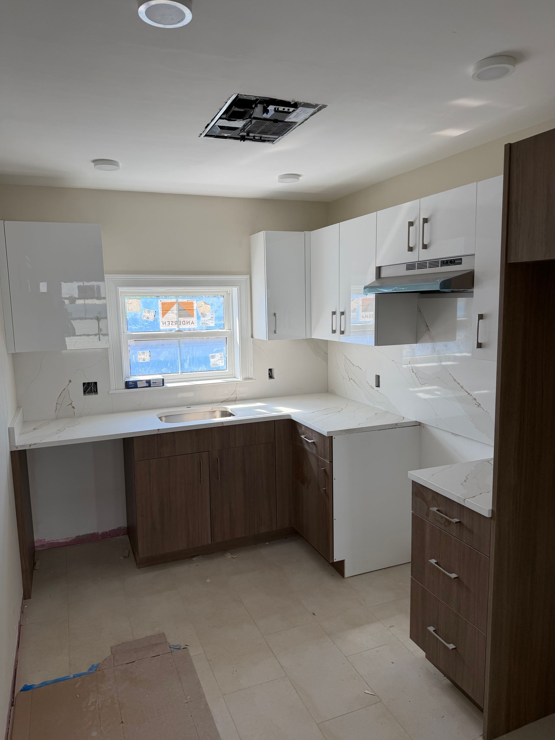 Bright kitchen under renovation with white cabinets, tiled floor, and a window over the sink.