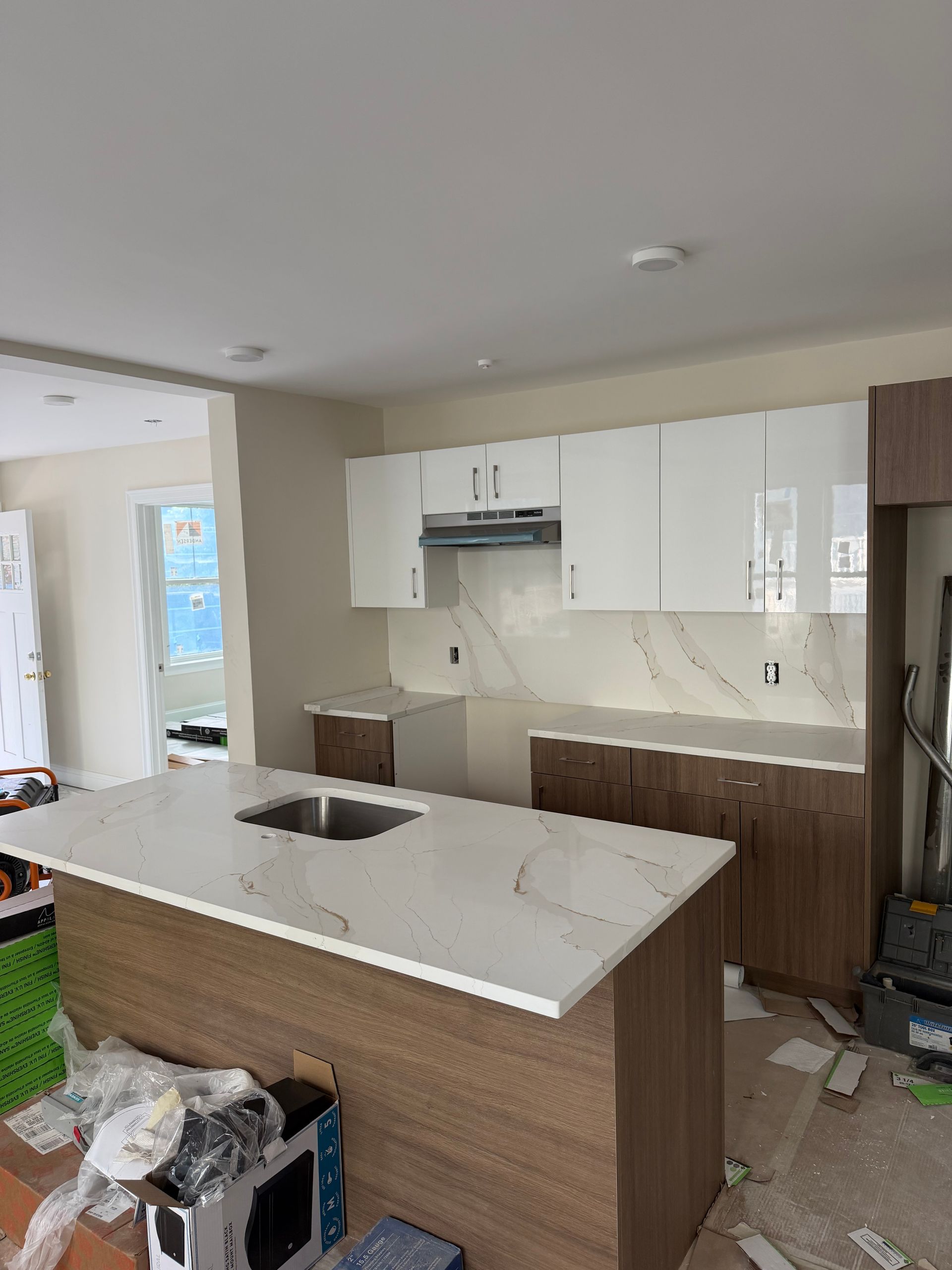 Modern kitchen with white cabinets, wood island, and marble countertops in a partially unfinished room