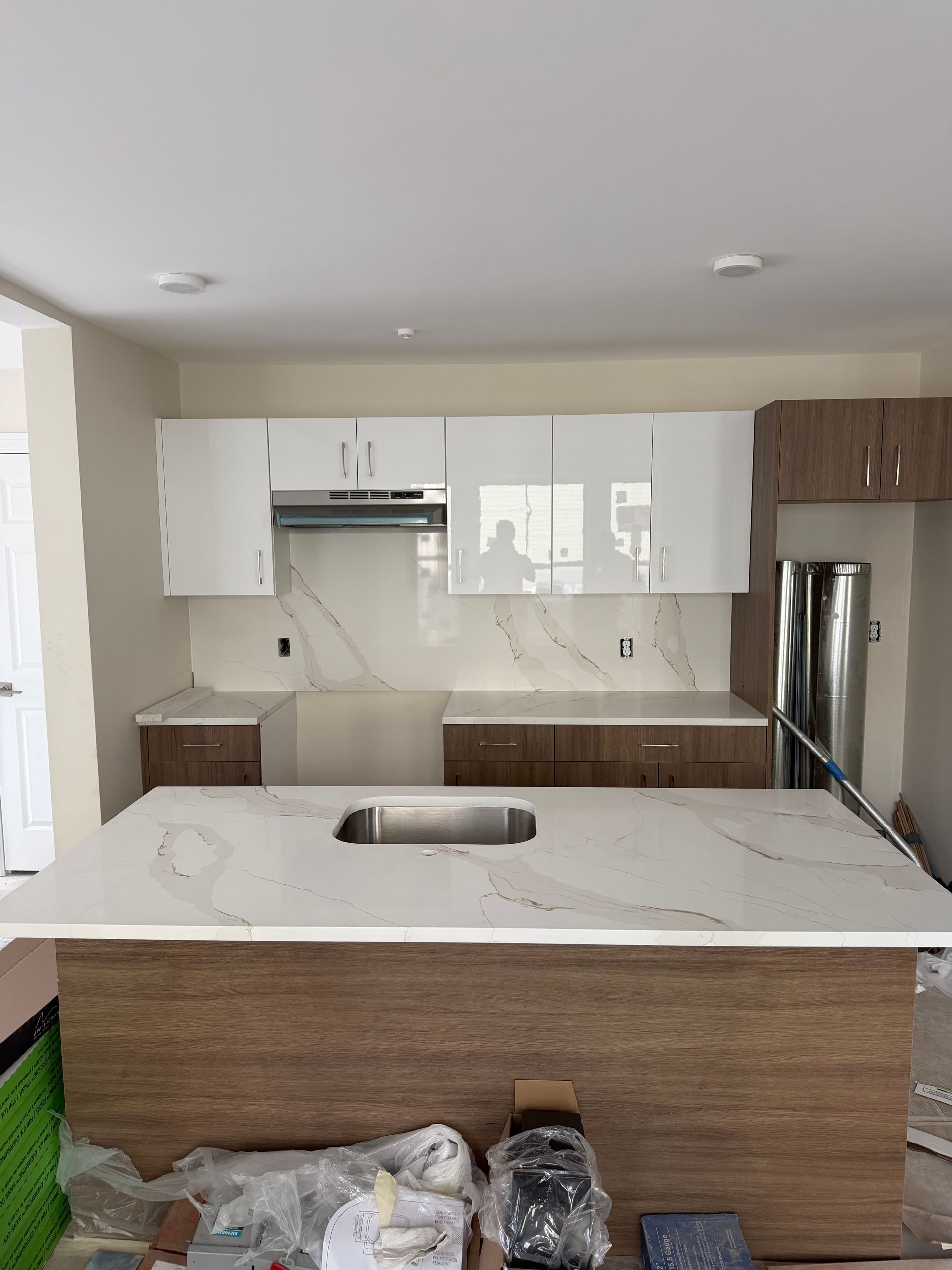 Modern kitchen with white cabinets, marble island, wood accents, and stainless steel refrigerator