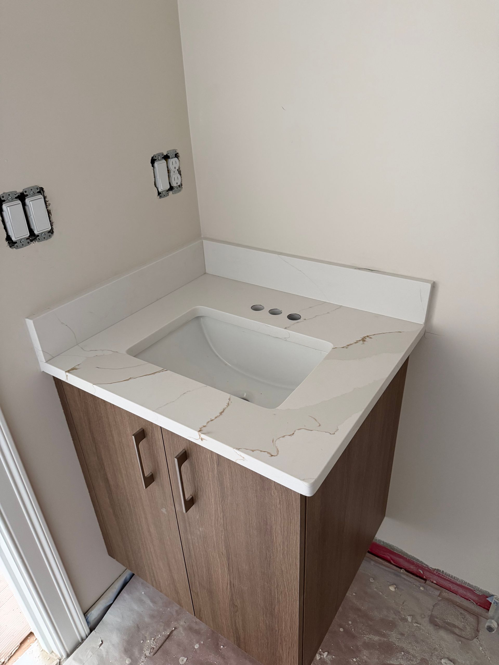 Bathroom vanity with a white sink and countertop over a wood cabinet, against an unfinished wall.