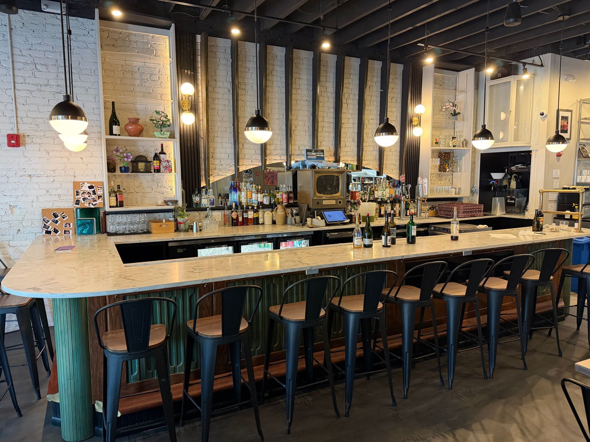 Stylish bar interior with wood counter, hanging pendant lights, and tall stools under black ceiling beams
